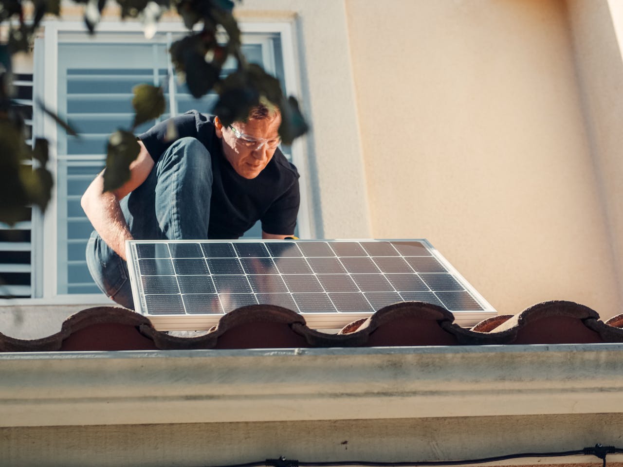 A Man in Black Shirt Installing a Solar Panel on the Roof